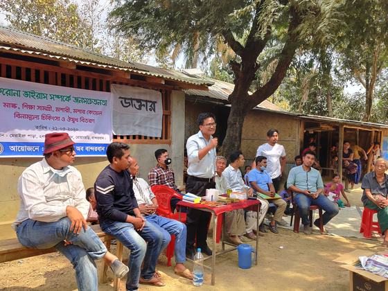 A doctor standing and addressing a seated audience in front of the camp banner