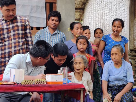 Two men leaning in to listen to an elderly woman seated beside the consultation table
