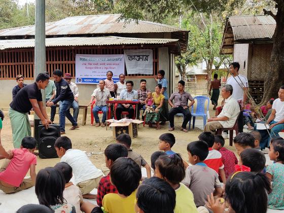 The gathering mid-session, children seated in the foreground and organisers at the table behind