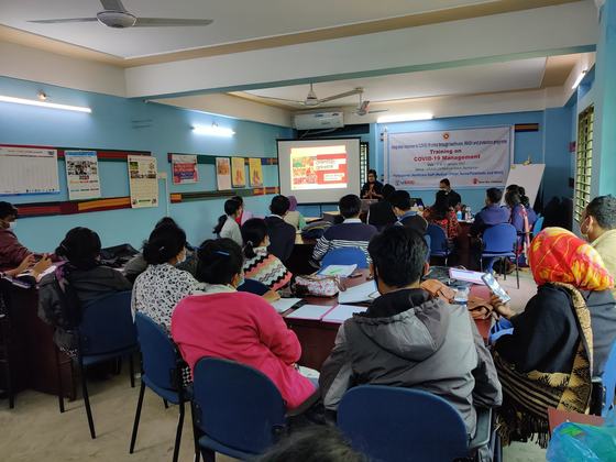 Healthcare staff seated at a COVID-19 management training session, facing a projected slide