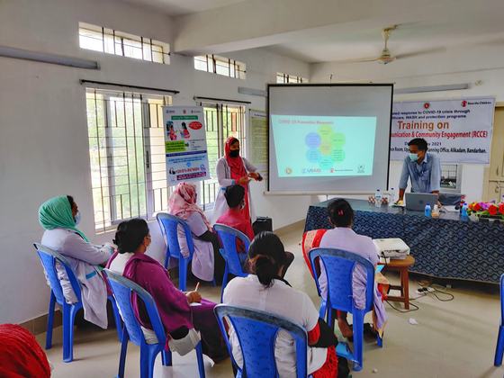 A participant standing beside a slide on COVID-19 preventive measures, addressing the room