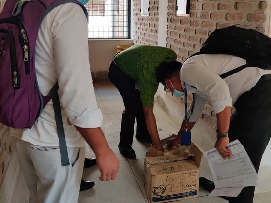 Staff opening a carton of examination gloves in a corridor while one holds the delivery paperwork