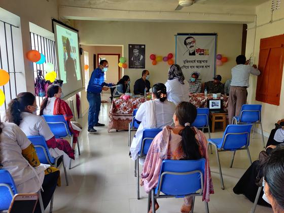 A briefing session with a projector screen and seated health staff at the family welfare centre