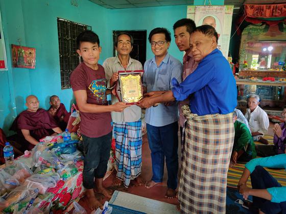 Community members handing over a commemorative plaque beside bagged relief supplies